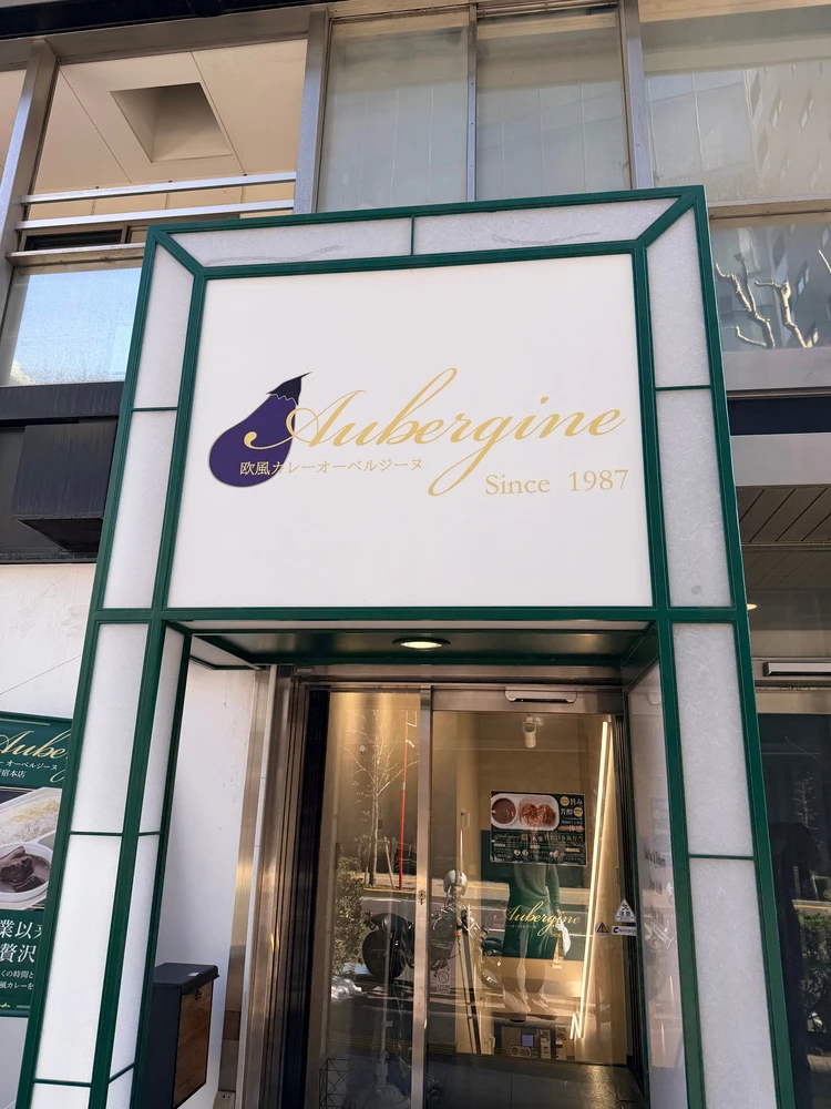 オーベルジーヌ新宿本店の入り口。新宿1丁目のビル（ソノリティ新宿御苑）の外観とテイクアウトの看板。