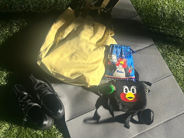 芝生にヨガマット、黒いスニーカー、HAYの黄色トートバック、つば九郎のミニポシェットとポーチが置かれている。