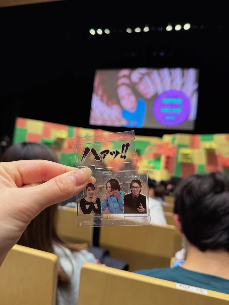 「ひっかかりニーチェ」イベント限定グッズの「アクリルスタンド」を手に持つ様子。