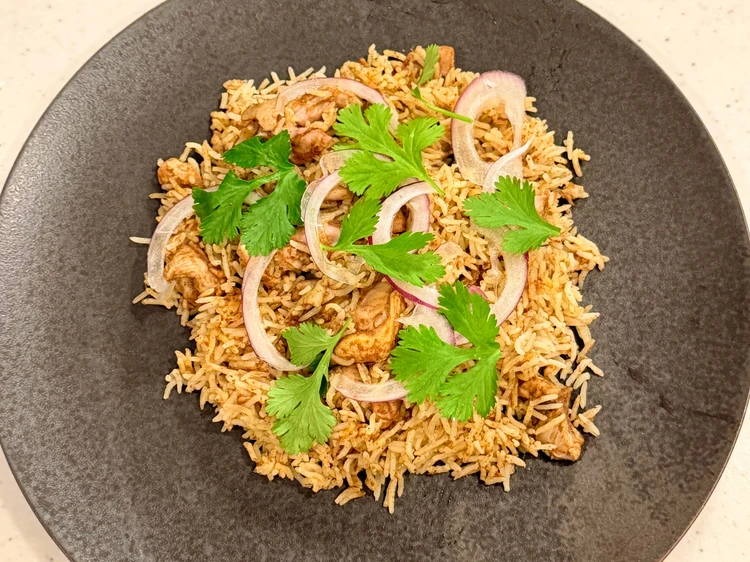 黒い皿に盛られたビリヤニ。パクチーと赤玉ねぎがのっている。