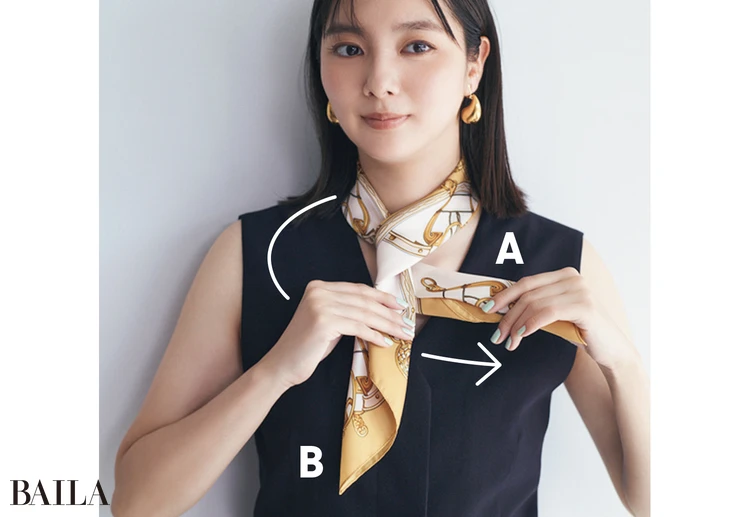 細くたたんだスカーフを首の前でクロス。そのまま上側Aを下側Bに巻きつけるように、後ろから一周させる。