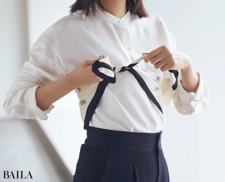 スカーフを対角線で三角に折り、両端を持って胸のあたりで結ぶ。前から見たときに三角の頂点が片足にかかるくらいまで、結び目を後ろにずらす。