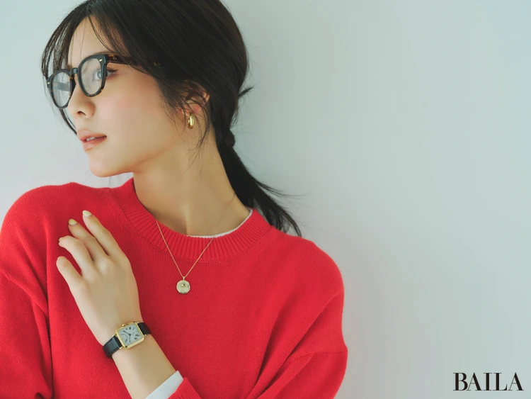 赤いニット、メガネ、ゴールドのピアスとネックレスを着用しているモデル写真